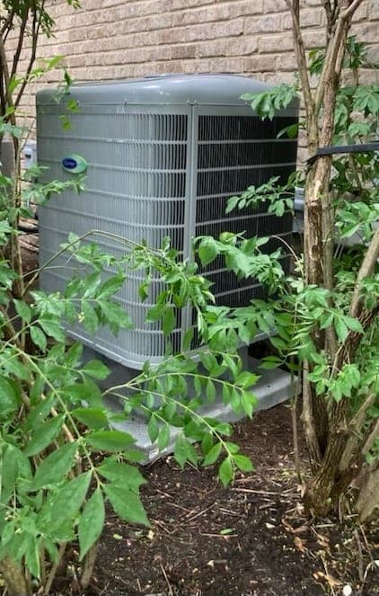 Carrier central air conditioner condenser installed on a pad beside a brick house
