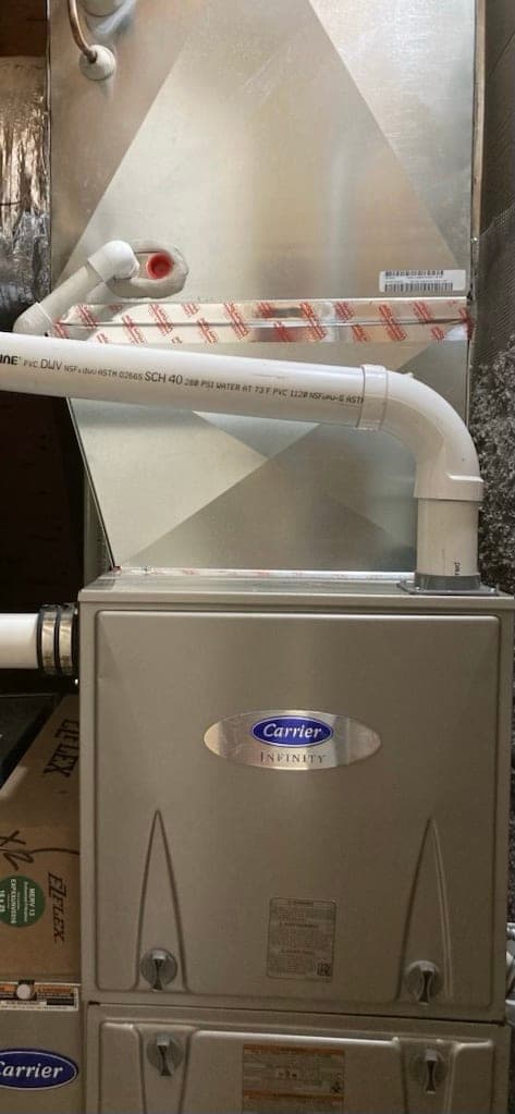 Carrier Infinity high-efficiency furnace with white PVC vent piping and a media filter cabinet